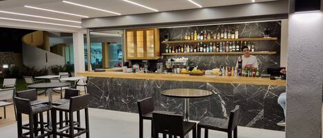 Un área de bar moderna con una encimera de mármol, sillas de mimbre y una amplia selección de botellas y copas.