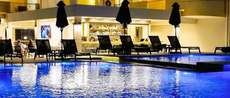 Uma área de piscina com espreguiçadeiras e guarda-sóis, um bar e uma área de bar com garrafas.