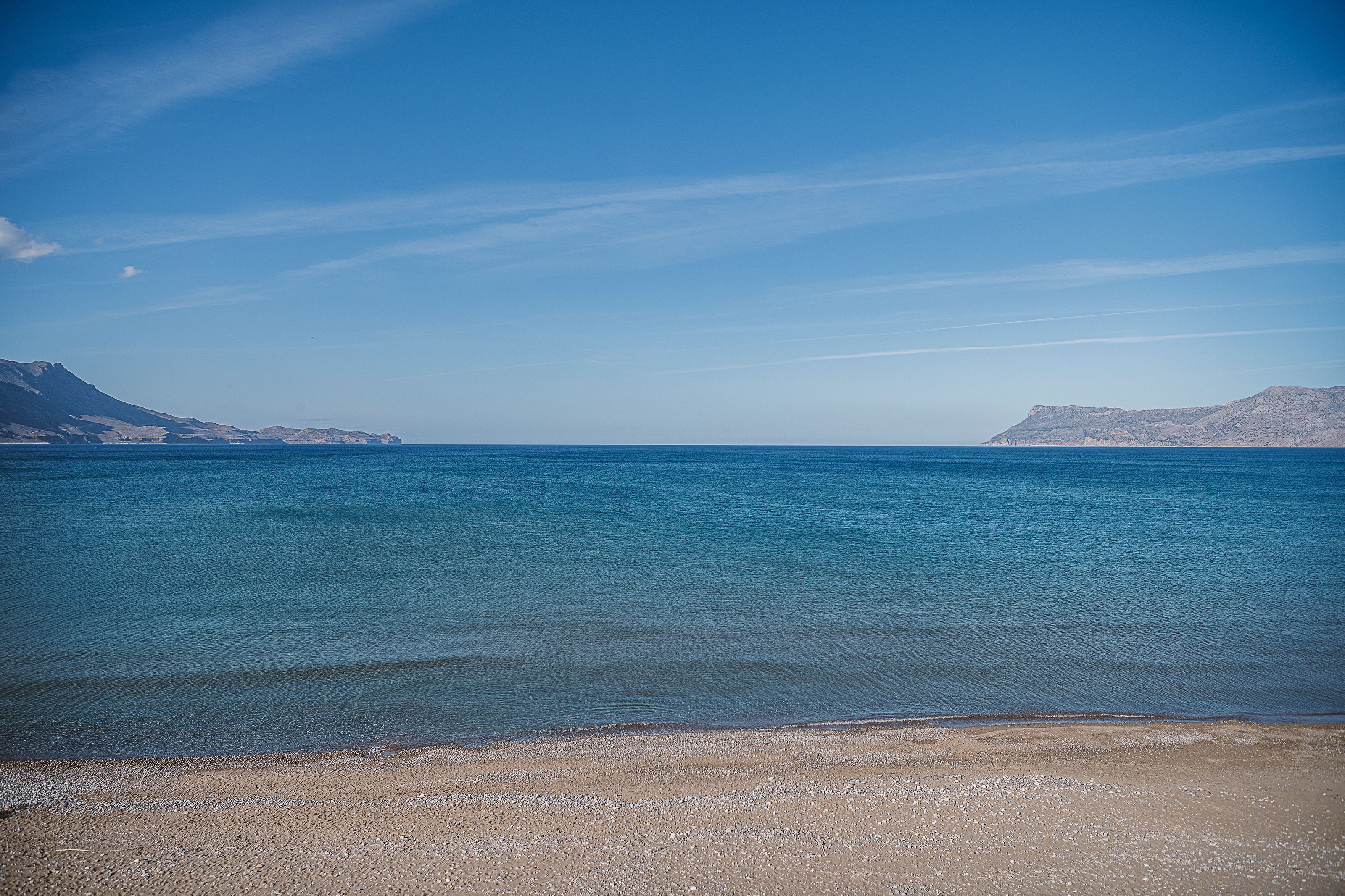 A beach with clear blue water and distant mountains.
