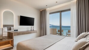 Habitación de hotel moderna con una cama grande, un televisor montado, un escritorio con una silla y un balcón con vistas al mar.