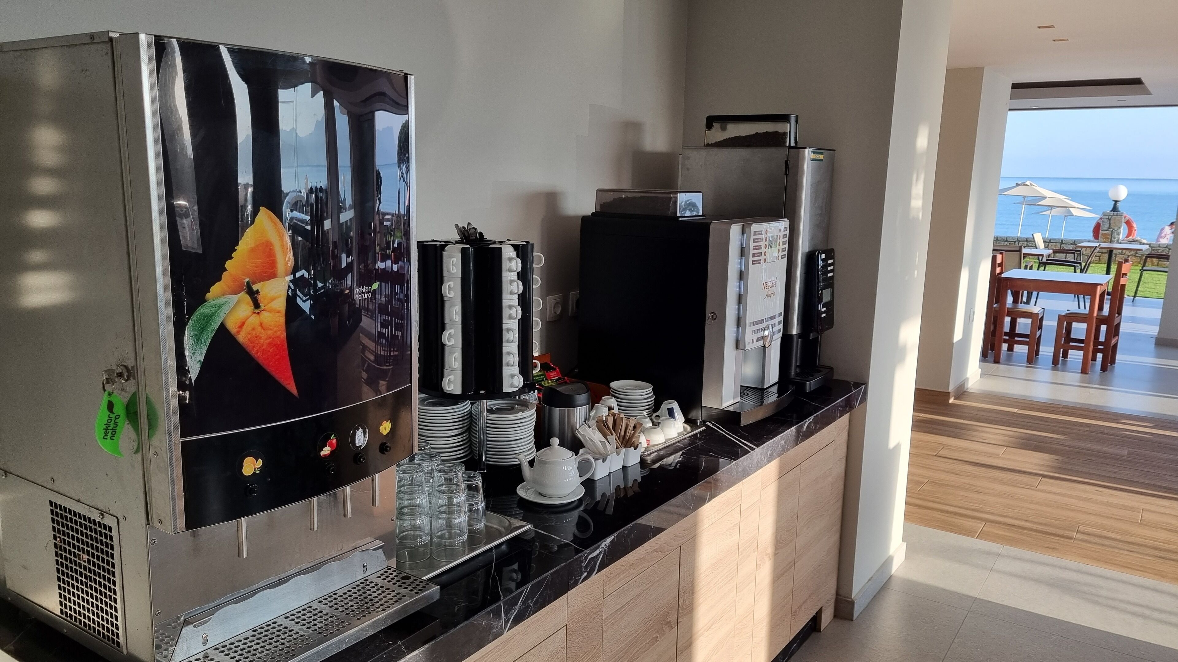 A kitchenette with a coffee machine, a refrigerator, and a view of the sea.
