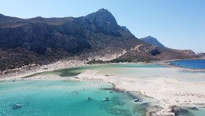 Un paisaje costero con una playa, aguas cristalinas y montañas al fondo.