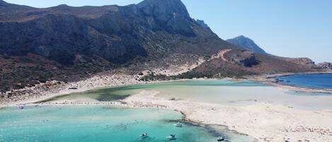 A coastal landscape with a beach, clear waters, and a mountainous backdrop.