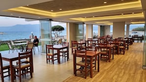 Un comedor espacioso con mesas y sillas de madera, ventanas amplias que ofrecen vista al mar y un diseño de techo moderno.