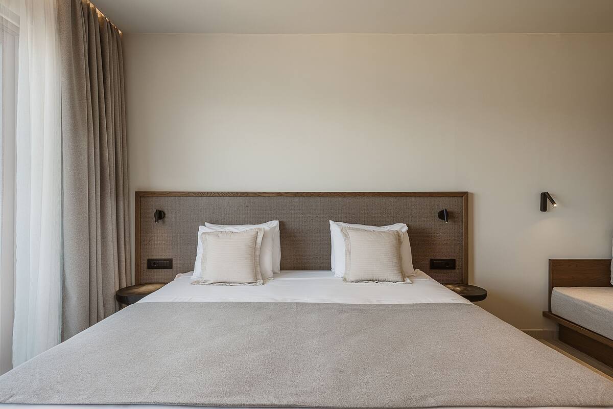 Une chambre d’hôtel avec un grand lit, deux tables de chevet, une tête de lit et une fenêtre avec des rideaux.