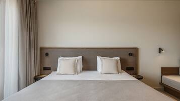 A hotel room with a large bed, two bedside tables, a headboard, and a window with curtains.