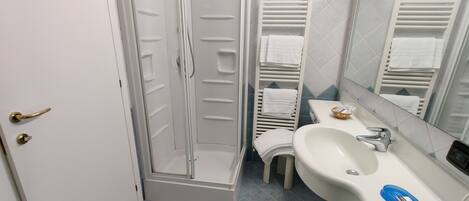 Un baño con ducha, lavamanos y perchero para toallas.