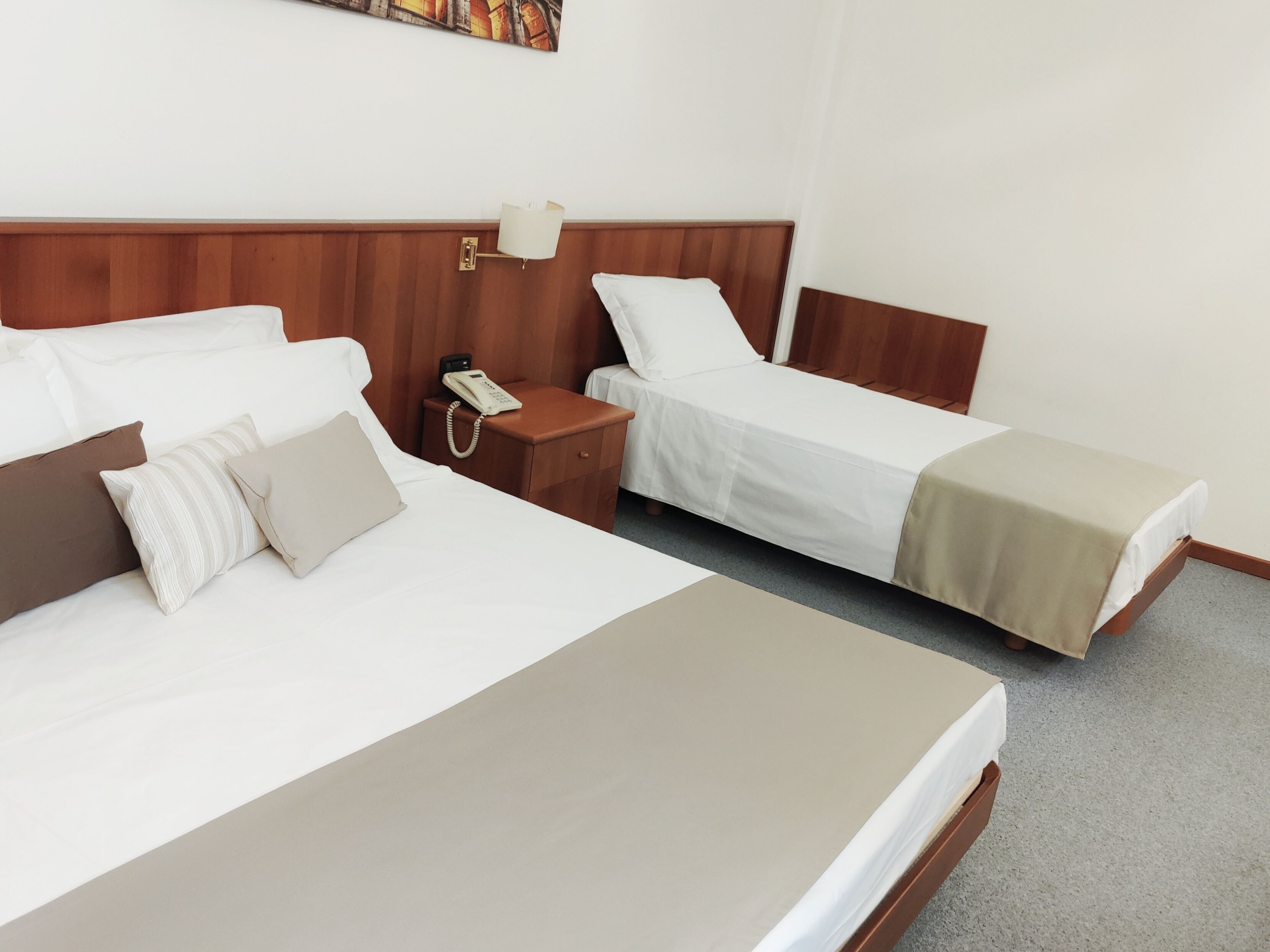 A hotel room with two beds, a bedside table with a lamp, and a phone.