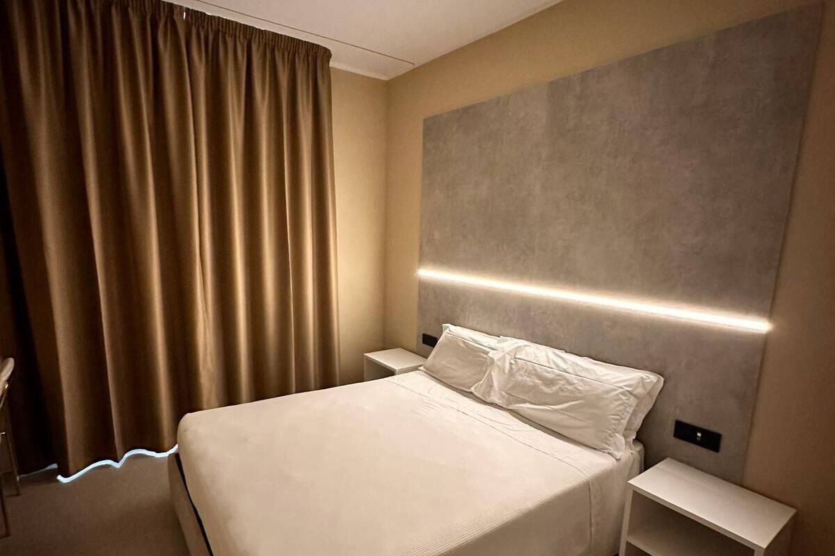 A modern hotel room with a large bed, bedside tables, and a headboard with integrated lighting.