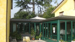 A conservatory with a green frame, a table with chairs, and potted plants. - Hotel Al Giardino (Treviso)