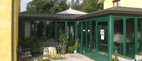 A conservatory with a green frame, a table with chairs, and potted plants.