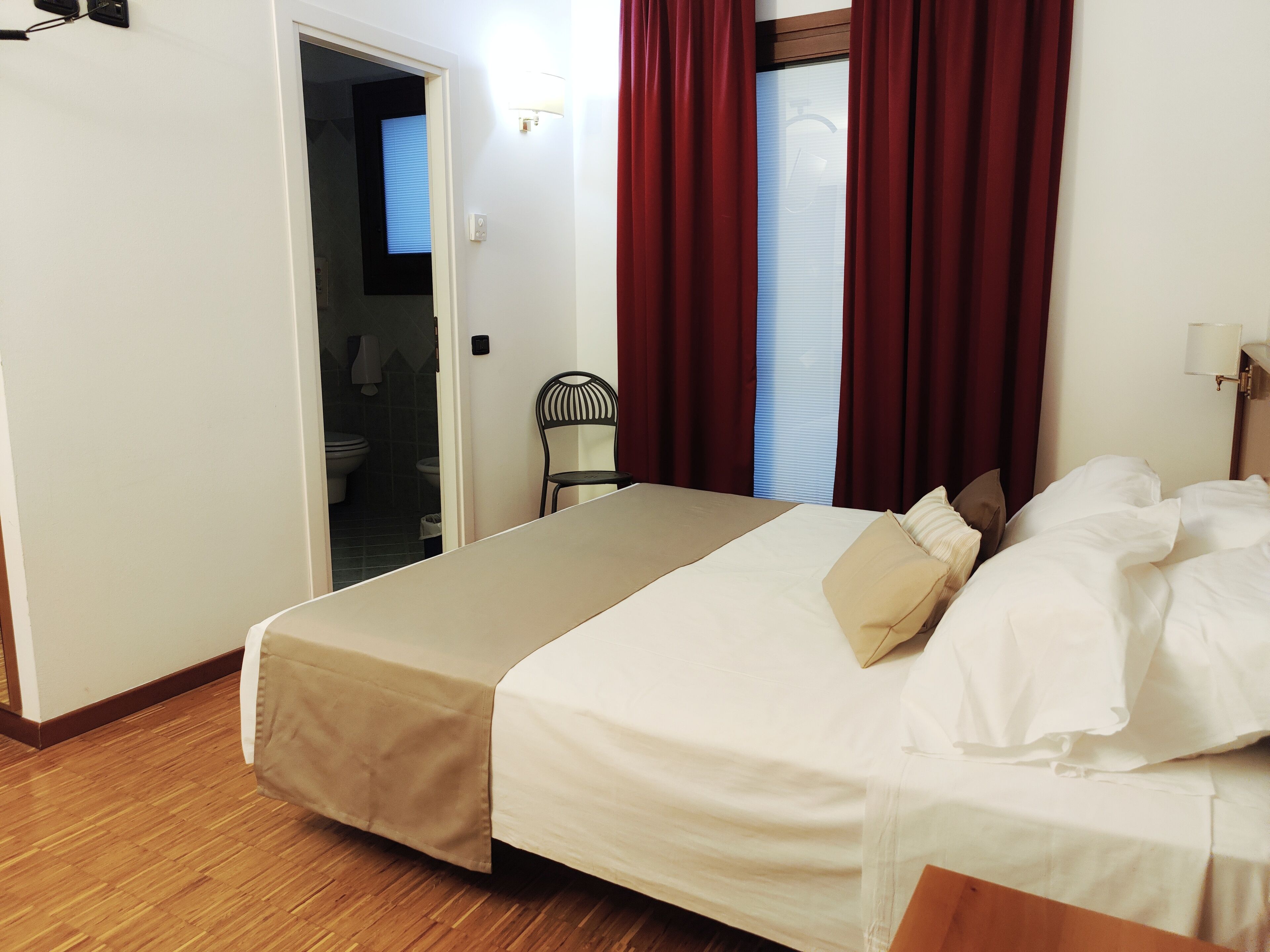 Habitación de hotel con cama, una silla, armario y baño visible a través de una puerta abierta.