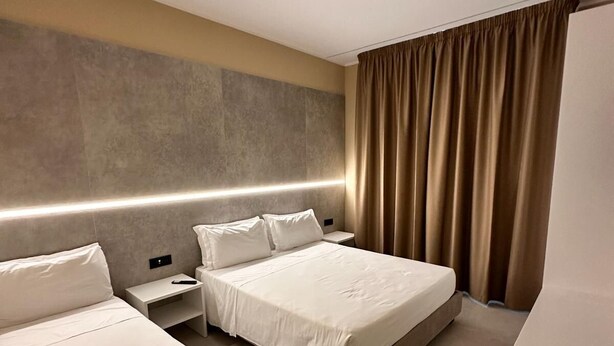 A hotel room with two beds, a bedside table, a nightstand, a large mirror, and a window with curtains. - Hotel Al Giardino (Treviso)