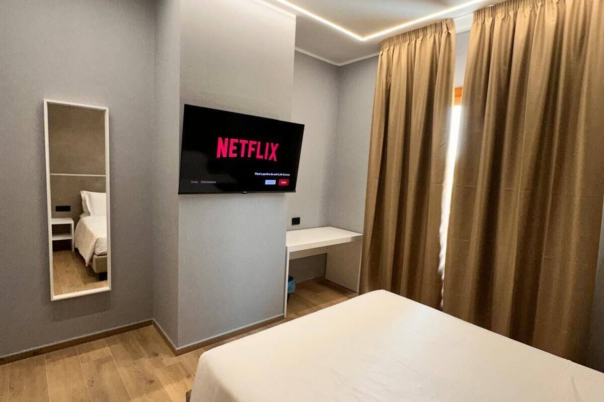 A hotel room with a bed, a desk, a TV displaying 'NETFLIX', and a mirror.