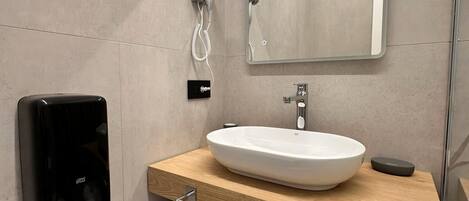 Un baño moderno con un espejo grande, un lavamanos blanco y un dispensador de toallas.