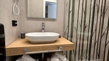 Ein modernes Badezimmer mit einem Holzkosmetikschrank, einem weißen Waschbecken und einer Duschkabine aus Glas.
