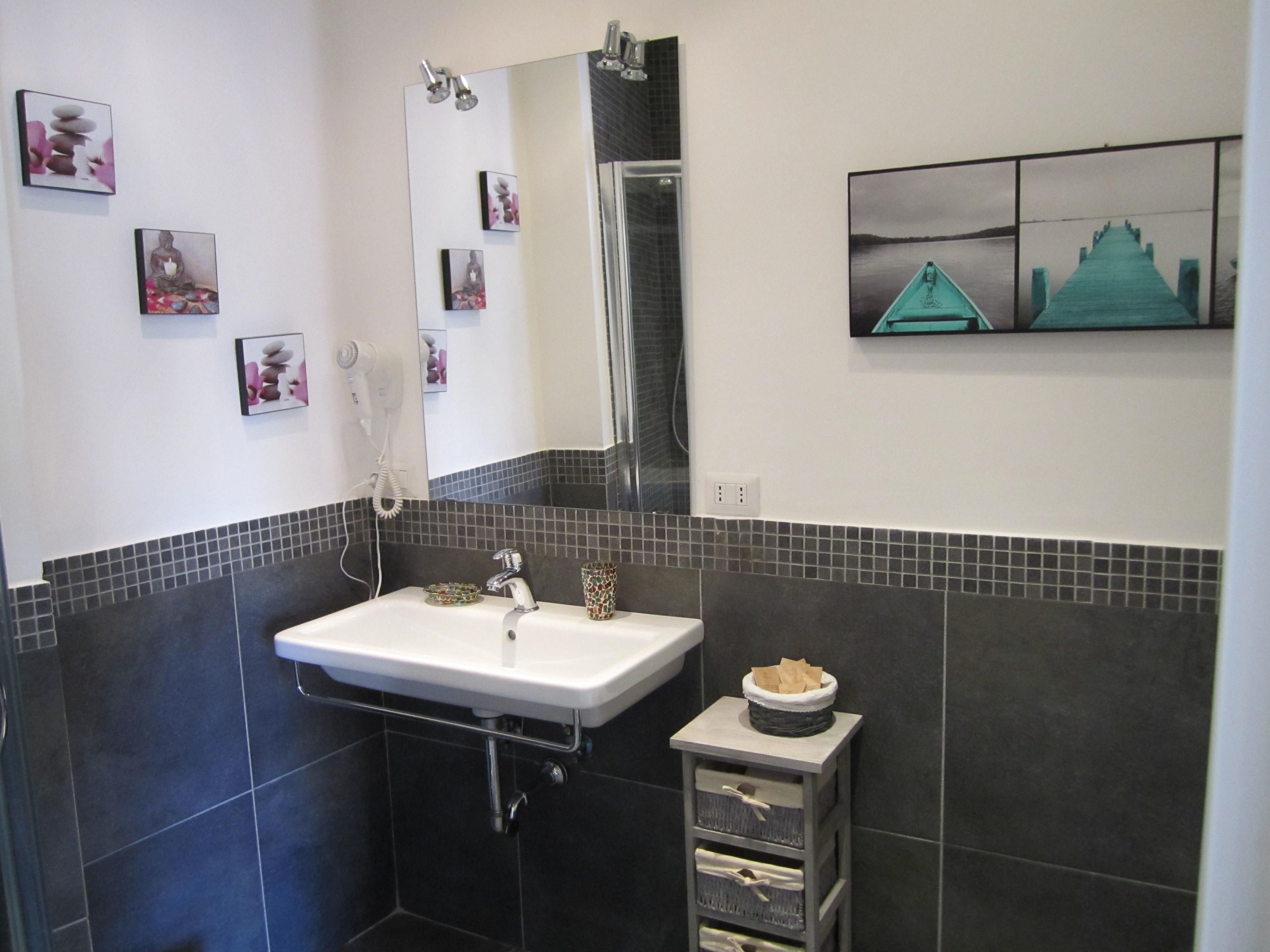 A modern bathroom with a white sink, dark tiled walls, a mirror, and a small cabinet with a tissue holder.
