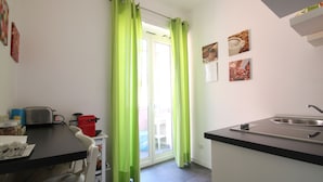 Una cuina compacta amb zona de menjador, una finestra amb cortines verdes i un rentapeus.