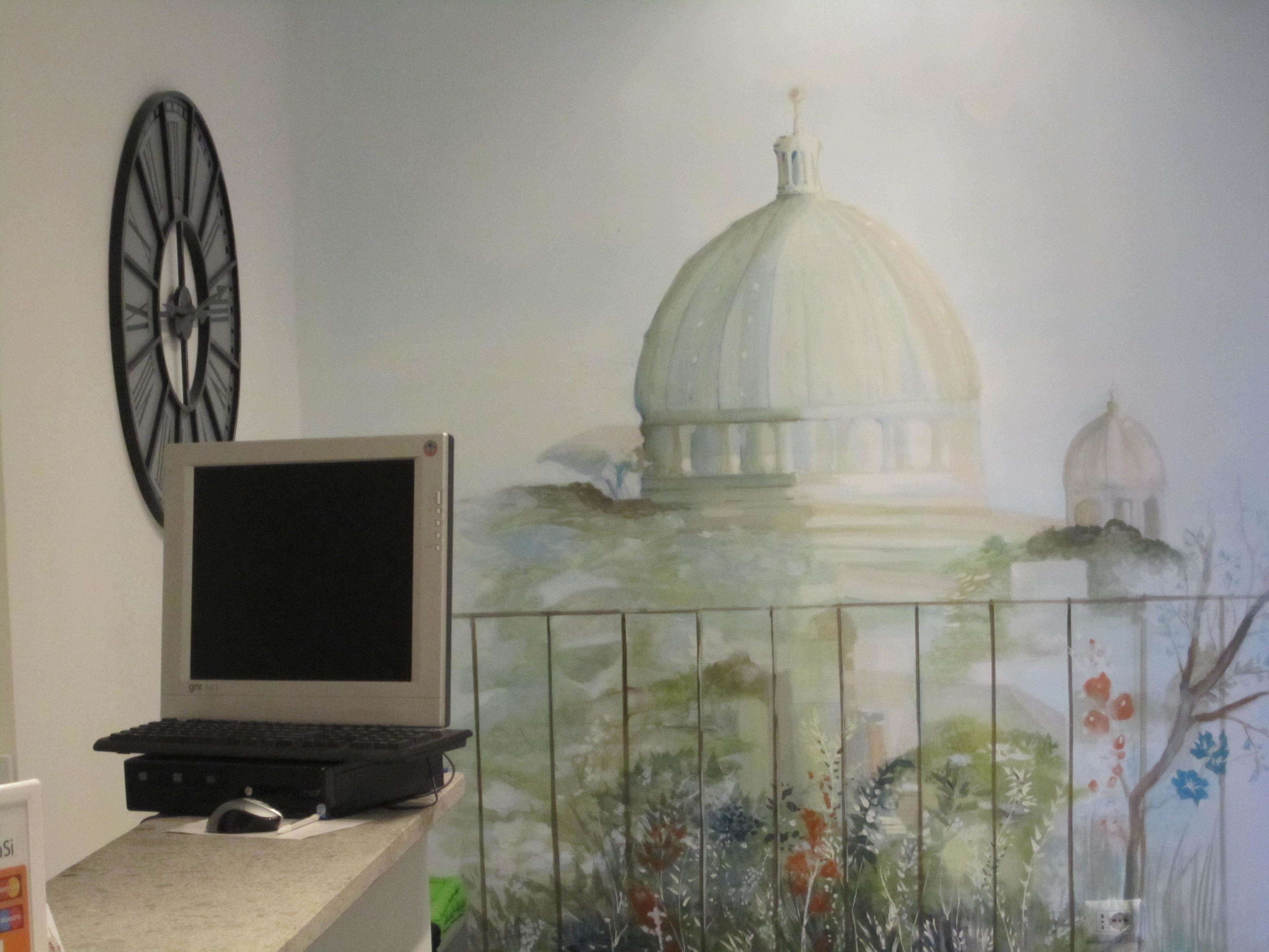 A room with a desk, a laptop, a wall clock, and a mural of a building.