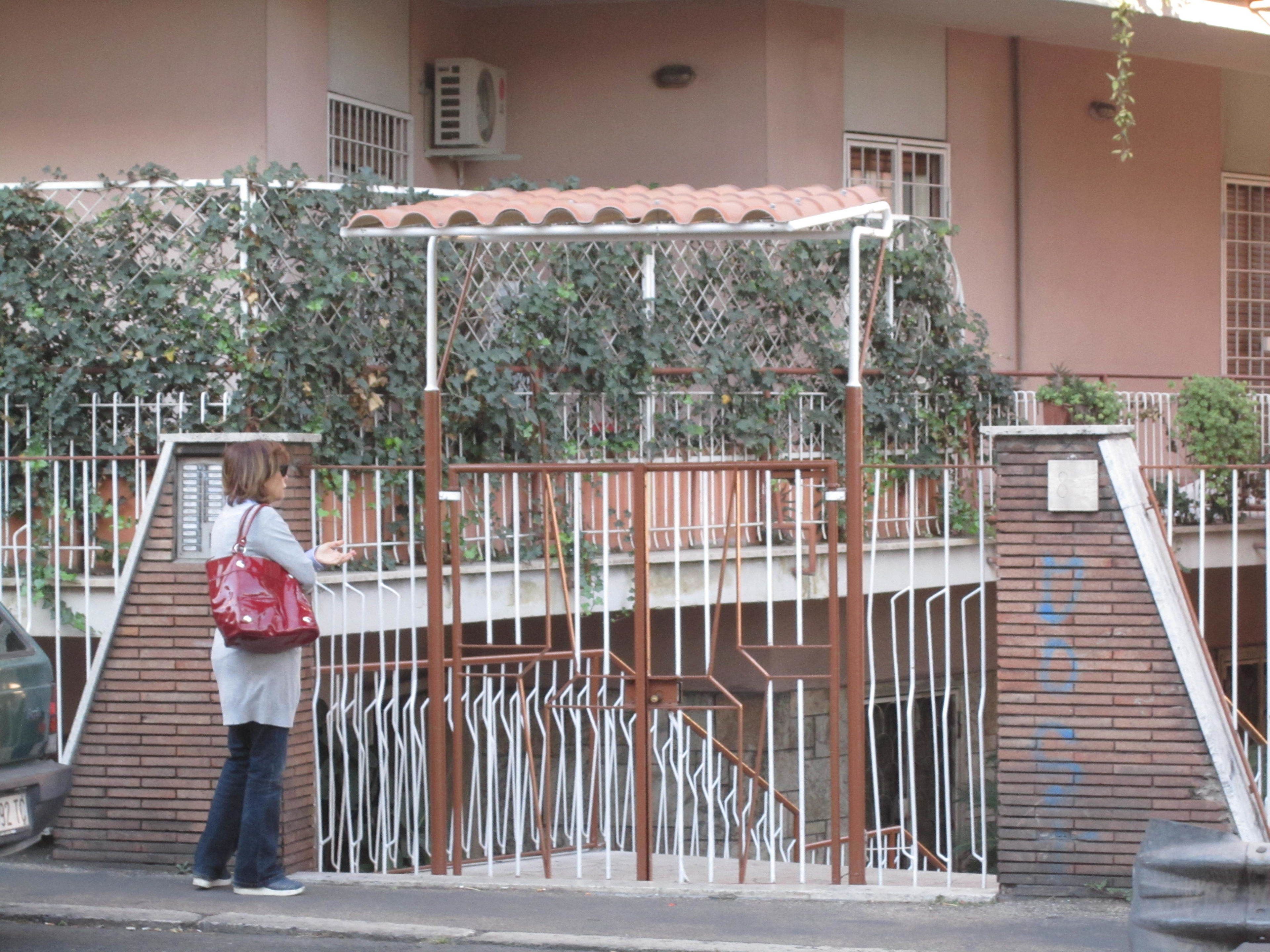 A person standing in front of a gated entrance with a metal fence and a brick wall.