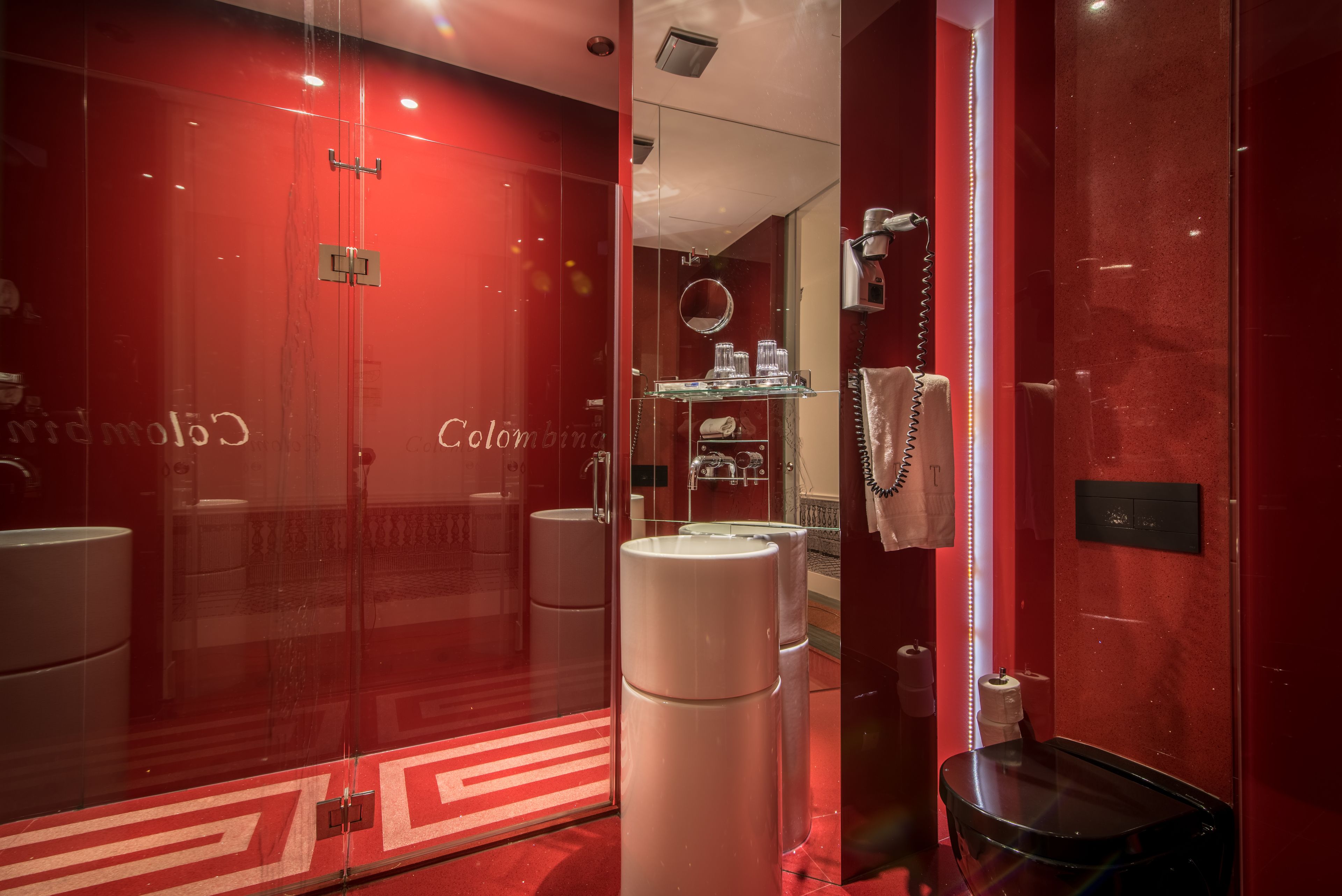 Een moderne badkamer met een rood thema, met een douchecabine van glas, een zwarte wastafel en een spiegel.