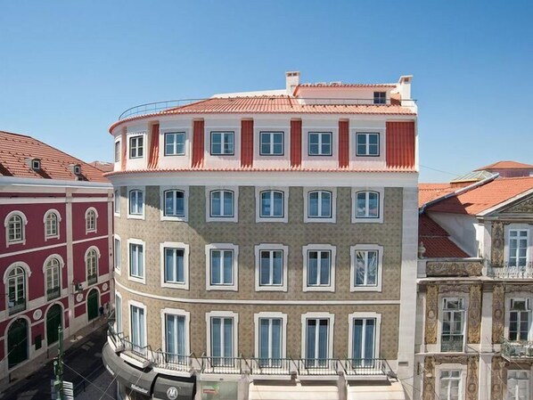 Un immeuble à plusieurs étages présentant un mélange de styles architecturaux, avec une combinaison de façades rouges et beiges, de nombreuses fenêtres et un angle incurvé.