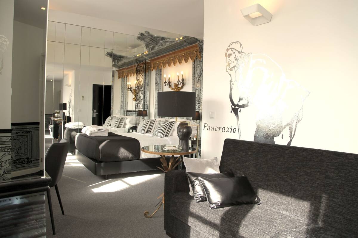 Ein modernes Hotelzimmer mit einem großen Bett, einer Couch, einem Glastisch und einem an der Wand montierten Fernseher.