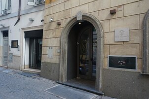 Un edificio in pietra con un ingresso ad arco, una targa con su scritto "Hotel Manfredo 12 Roma" e un cartello che indica "Fire Glass".