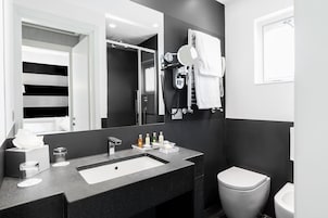 Een moderne badkamer met een grote spiegel, een wastafel met toiletartikelen, een handdoekrek en een toilet.