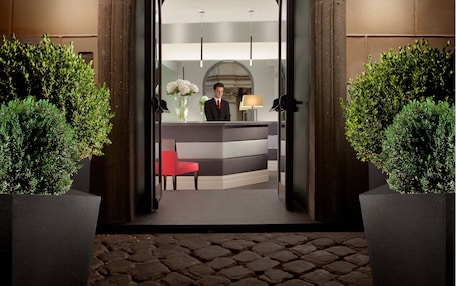 A hotel reception area with a receptionist, a reception desk, and a large arched doorway.
