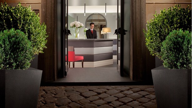 A hotel reception area with a receptionist, a reception desk, and a large arched doorway. - Hotel Mancino 12 (Rome)