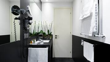 Un baño moderno con una paleta de colores blanco y negro, un secador de pelo, un lavabo con artículos de aseo y un espejo.