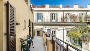 A narrow outdoor corridor with a table and chairs, a closed shutter door, and a view of adjacent buildings. - Hotel Mancino 12 (Rome)