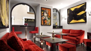 A modern interior with red upholstered furniture, a black and yellow abstract painting, and a visible logo on the wall. - Hotel Mancino 12 (Rome)