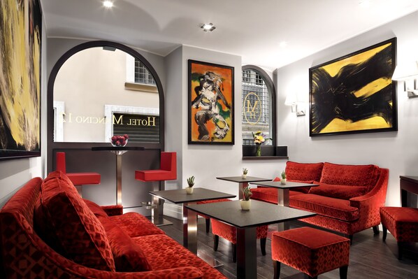 Un interior moderno con mobiliario tapizado en rojo, un cuadro abstracto negro y amarillo, y un logotipo visible en la pared.