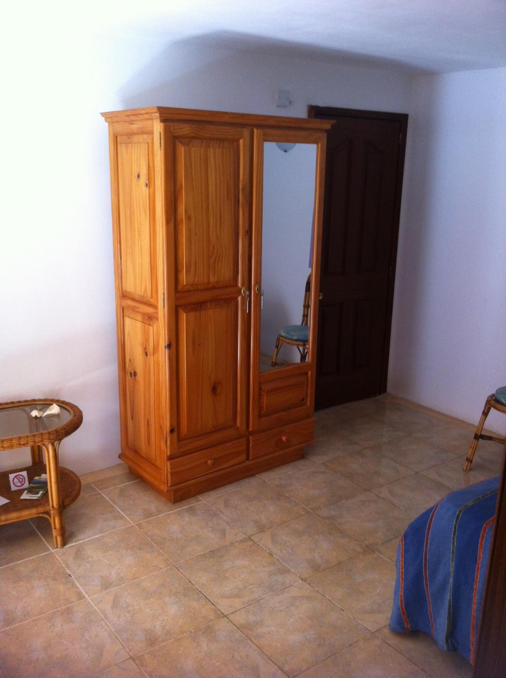 A room with a wooden wardrobe, a small table, and a chair.
