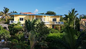 A two-story building with a yellow facade and blue roof, surrounded by lush tropical vegetation. - Tibambari (Le Bouchon)