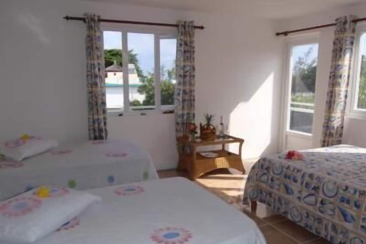 A room with two single beds, a small table with a chair, and a window with curtains.