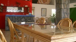 A dining area with a glass table, wicker chairs, a stone pillar, and a red wall with a mirror. - Tibambari (Le Bouchon)