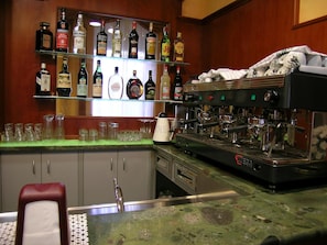Eine Bar mit Regalen voller Spirituosenflaschen, einer Kaffeemaschine und Gläsern auf der Theke.