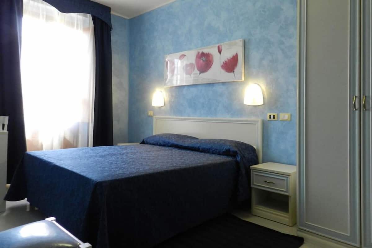 A bedroom with a bed, bedside tables, a wardrobe, and a painting on the wall.