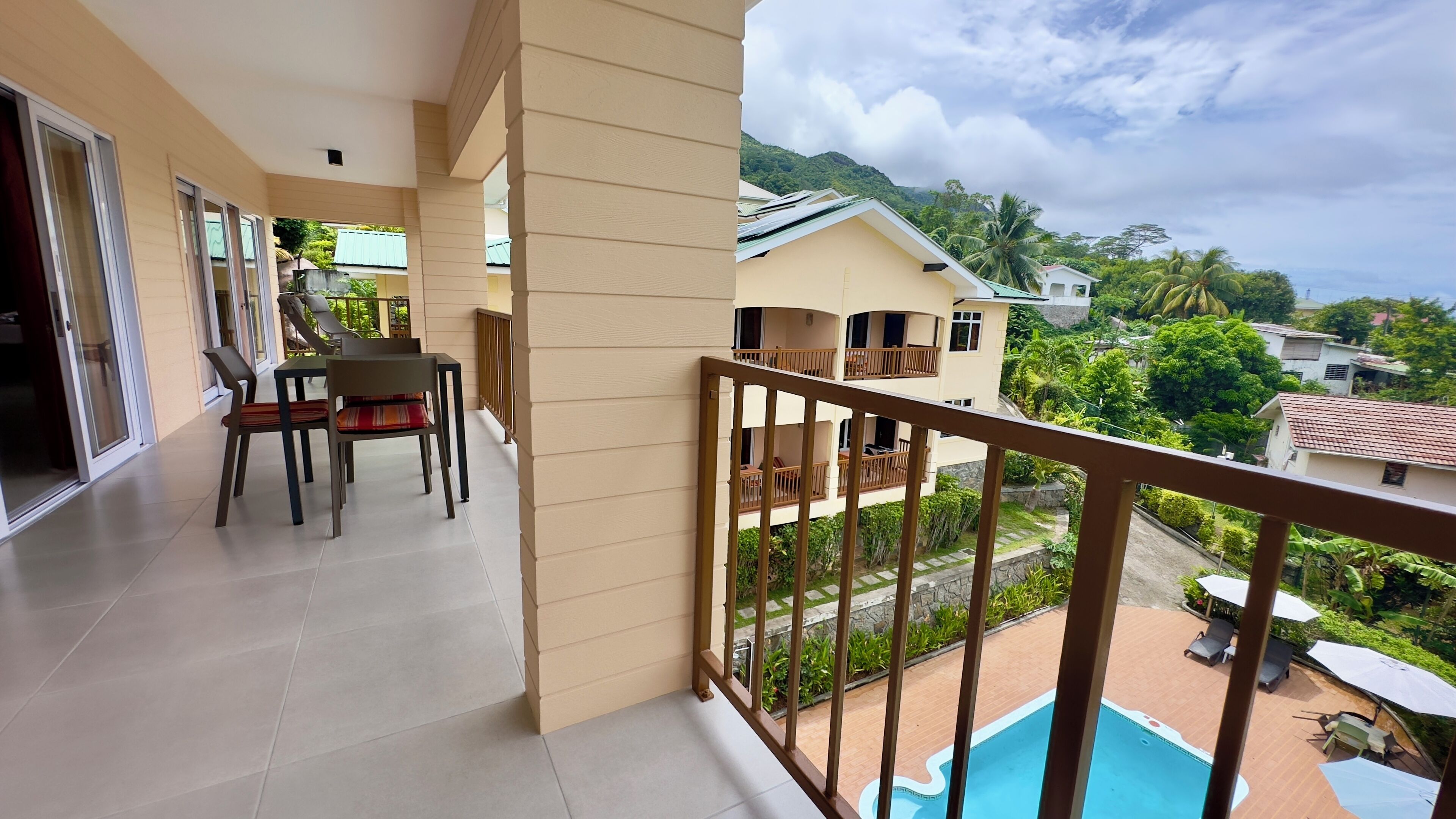 Un balcón con comedor, piscina y vista a un paisaje exuberante.