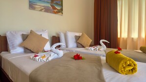 Une chambre d’hôtel avec deux lits, chacun recouvert d’une courtepointe blanche et agrémenté d’oreillers. On peut voir sur les lits des cygnes décoratifs faits avec des serviettes, et un tableau représentant une scène de plage est accroché au mur.