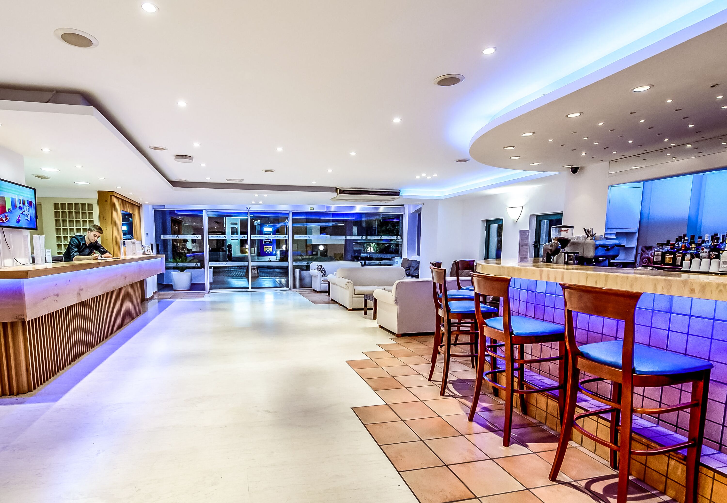 Un hall d’hôtel moderne comprenant un comptoir d’accueil, un espace salon et un bar.