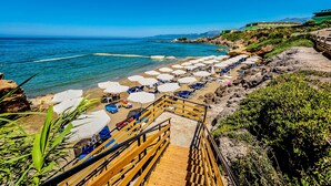 Ein Strand mit Holzstufen, die zum Ufer führen, weißen Sonnenschirmen und blauen Liegestühlen.