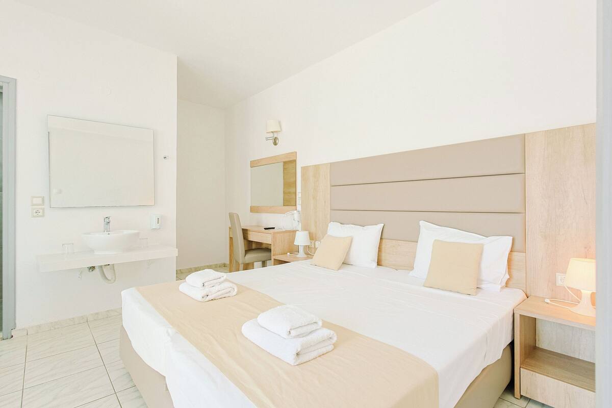 Une chambre d’hôtel comprenant un lit, un bureau, une chaise, une table de chevet et une salle de bain avec un lavabo et un miroir.