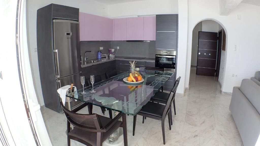 A modern kitchen with a glass dining table, dark cabinets, and a fruit bowl.