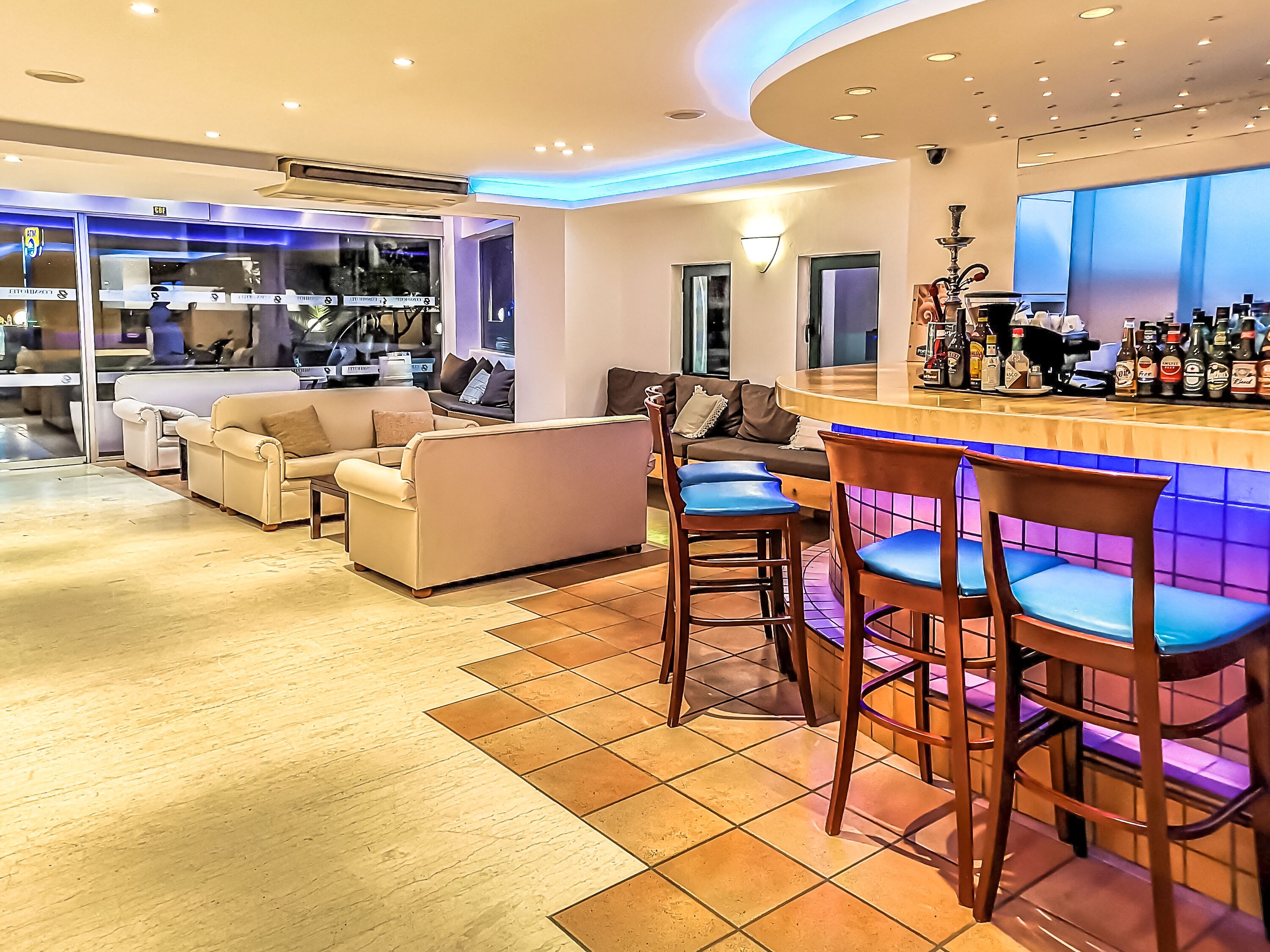 Un bar moderno con una barra curva, taburetes y una zona de estar con sofás y sillones.