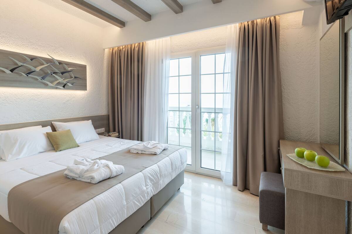 Une chambre d’hôtel avec un lit, un bureau avec un ordinateur portable et un balcon avec des rideaux.