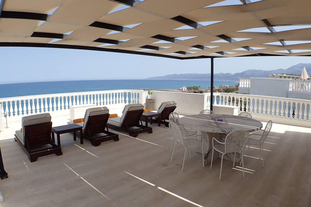 Un espace extérieur abrité, aménagé avec une table et des chaises, et offrant une vue sur la mer.